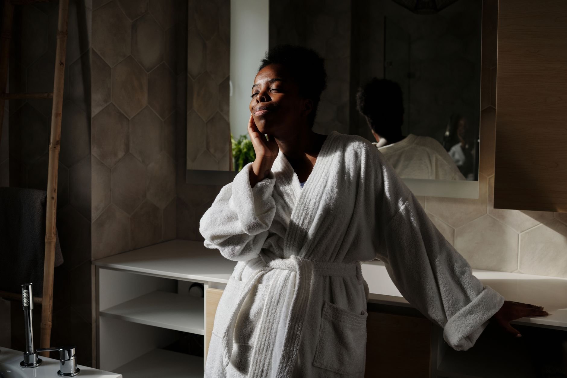 African American woman in a cozy white bathrobe, embracing a tranquil morning in her bathroom.